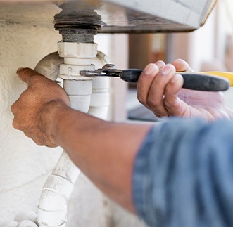 plumber's hands using a tool to adjust a white pipe under a sink